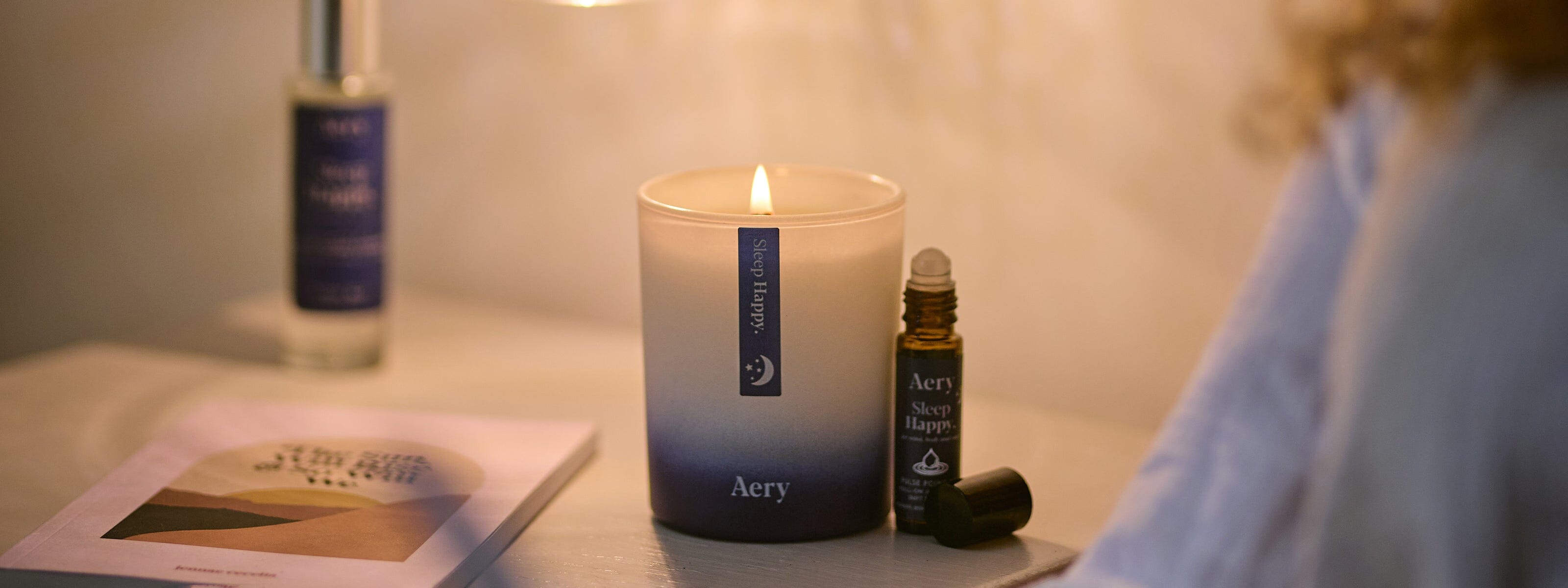 bedside table setting with sleep happy candle lit and sleep happy pulse point roll on