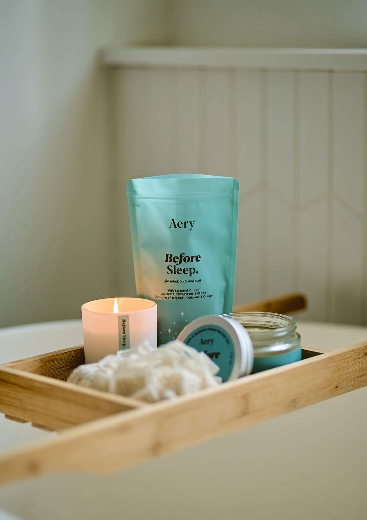 Blue Before Sleep bath salts pouch displayed with Before Sleep candle and bath salts jar placed on wooden bath tray in bathroom