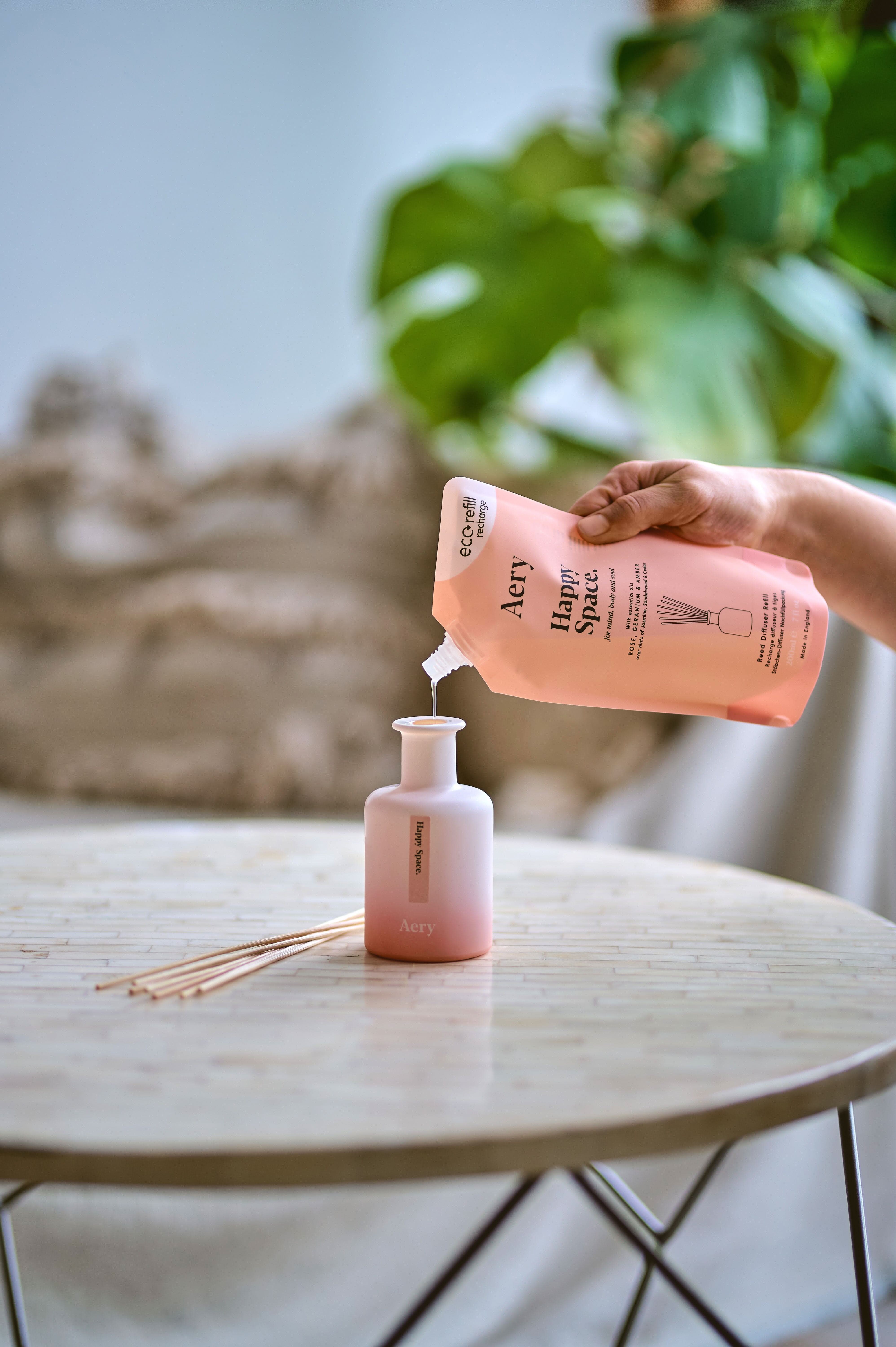 Happy Space reed diffuser refill pouch being poured into diffuser vase on circle table