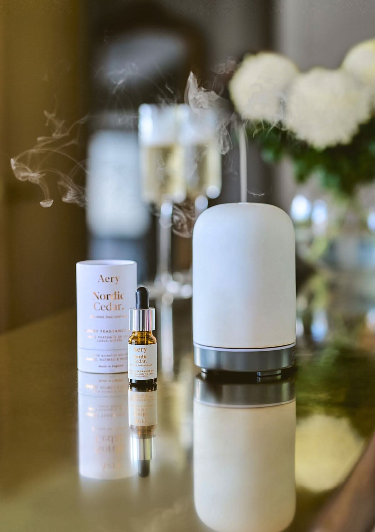 White Nordic Cedar fragrance oil by Aery displayed next to product packaging and electric diffuser placed on gold kitchen worktop
