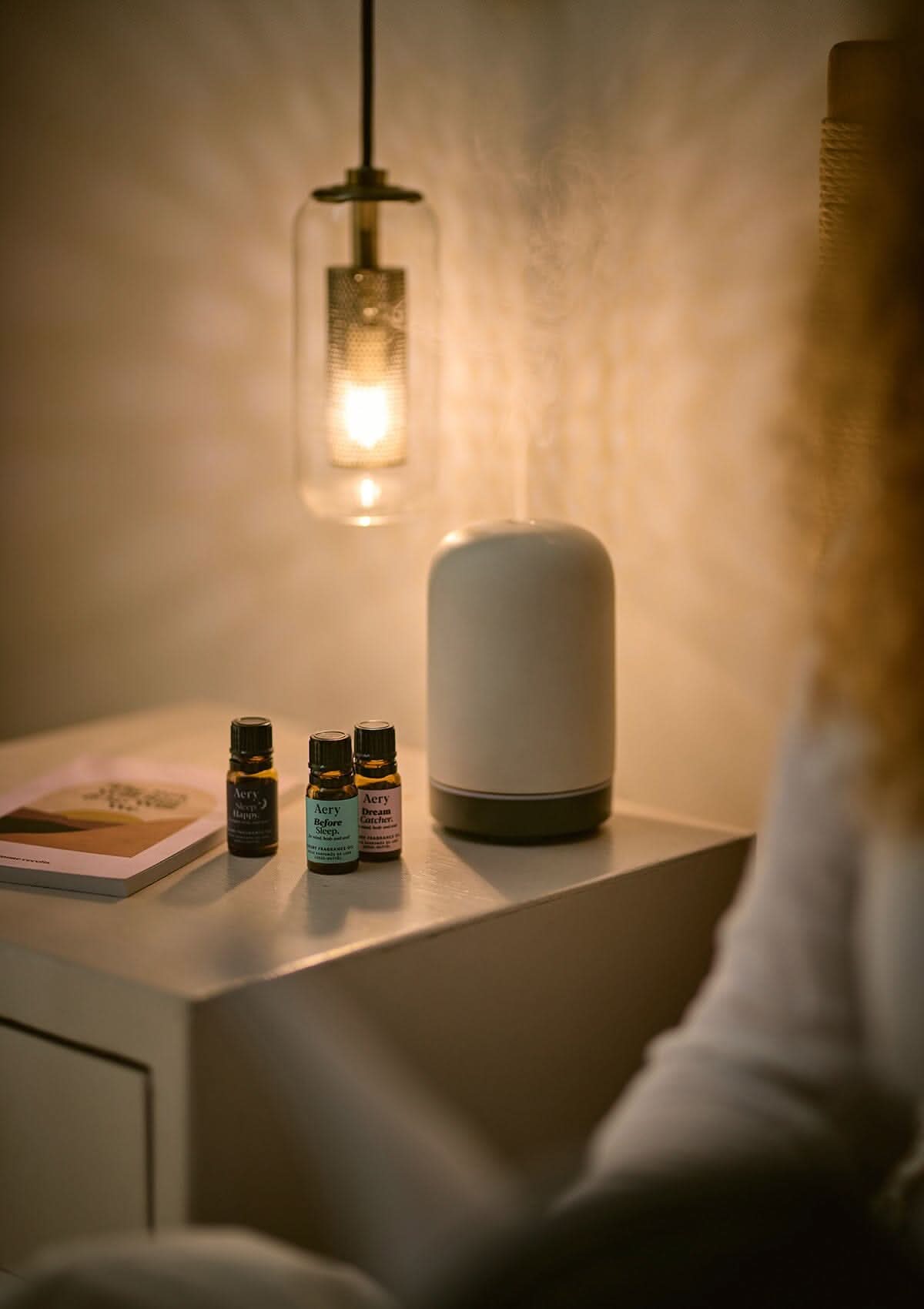 Sleep Therapy set of three fragrance oils by Aery displayed next to electric diffuser and book on bedside table