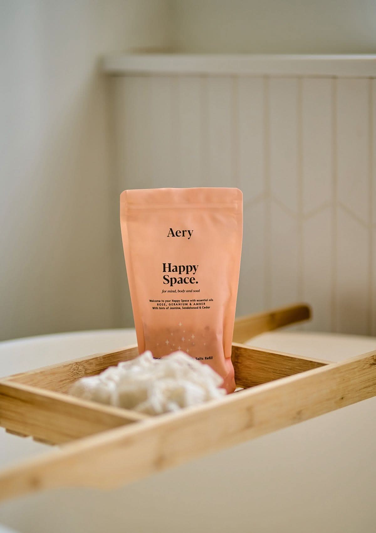 Pink Happy Space bath salts pouch displayed on wooden bath tray in bathroom