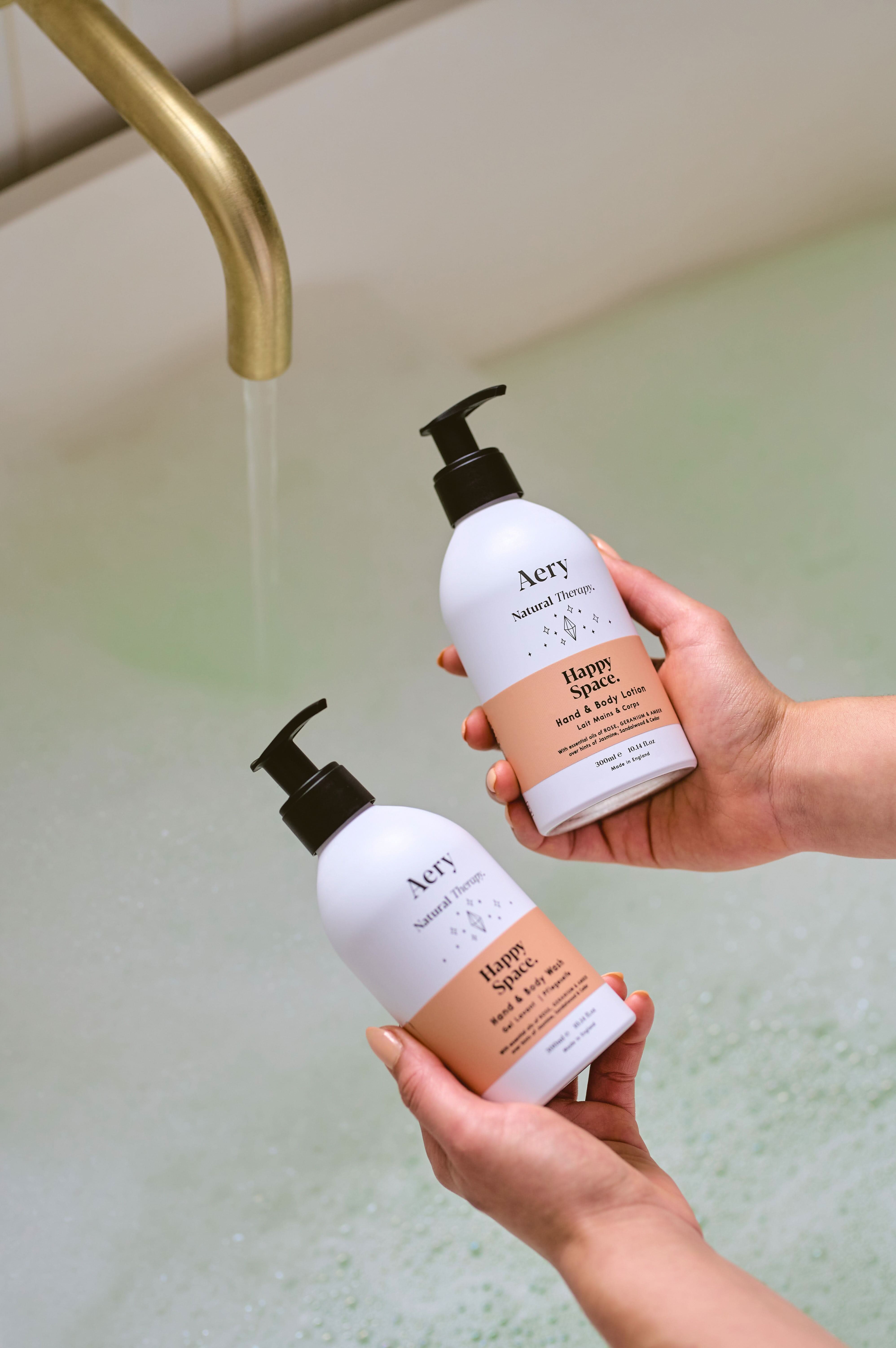 Pink Happy Space hand and body wash and lotion duo by Aery displayed in hands over bubble bath