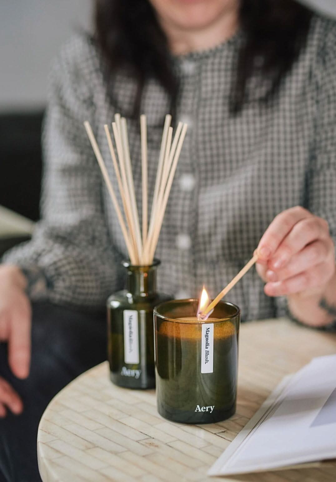 person lighting magnolia blush candle at a coffee table with matching reed diffuser