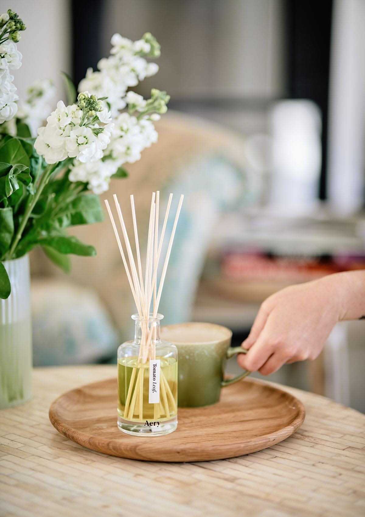 Tomato Leaf diffuser by Aery sat on wooden tray next to vase of white flowers