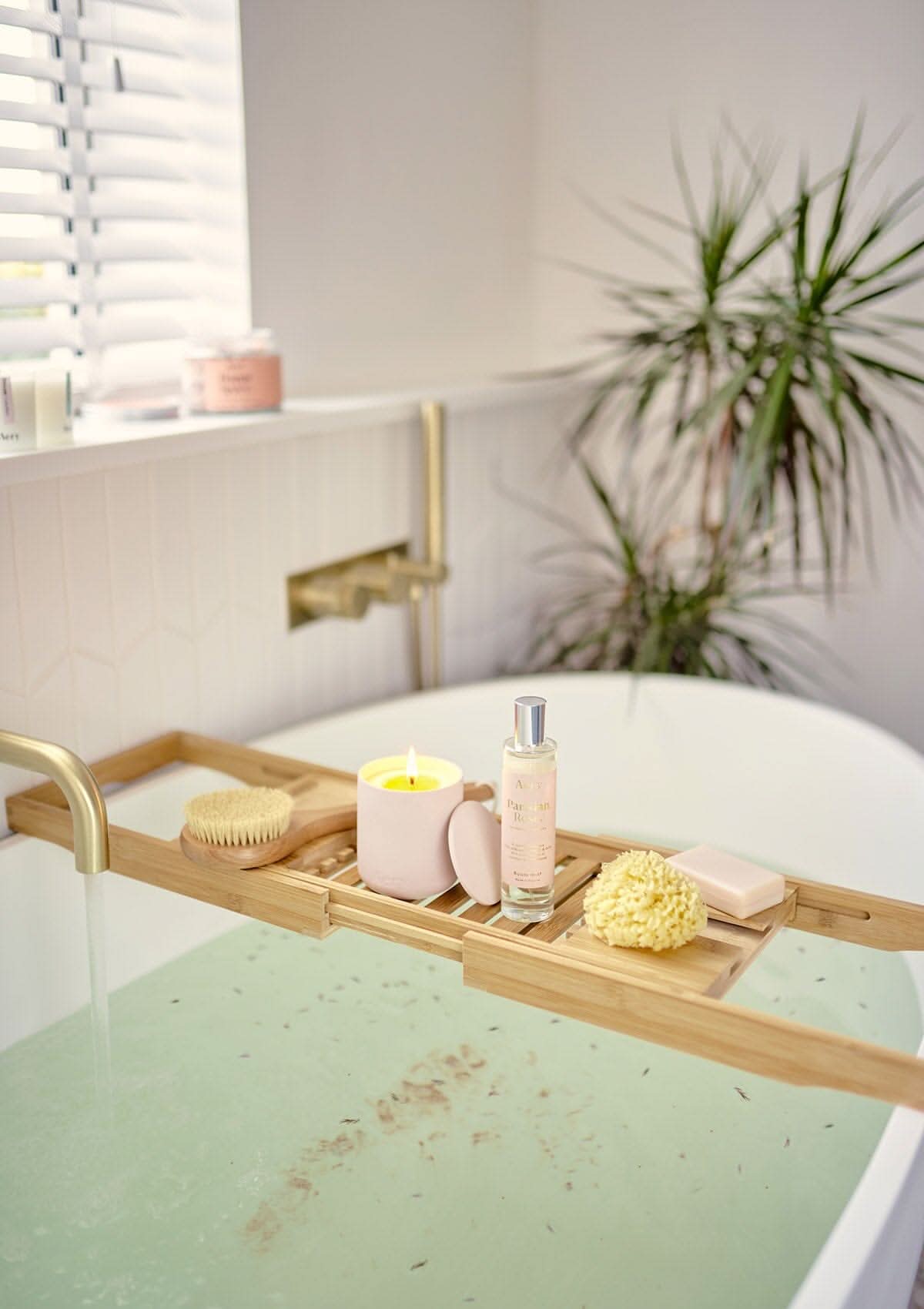Pink Parisian Rose candle displayed next to Parisian Rose room mist placed on wooden bath tray sat over bath