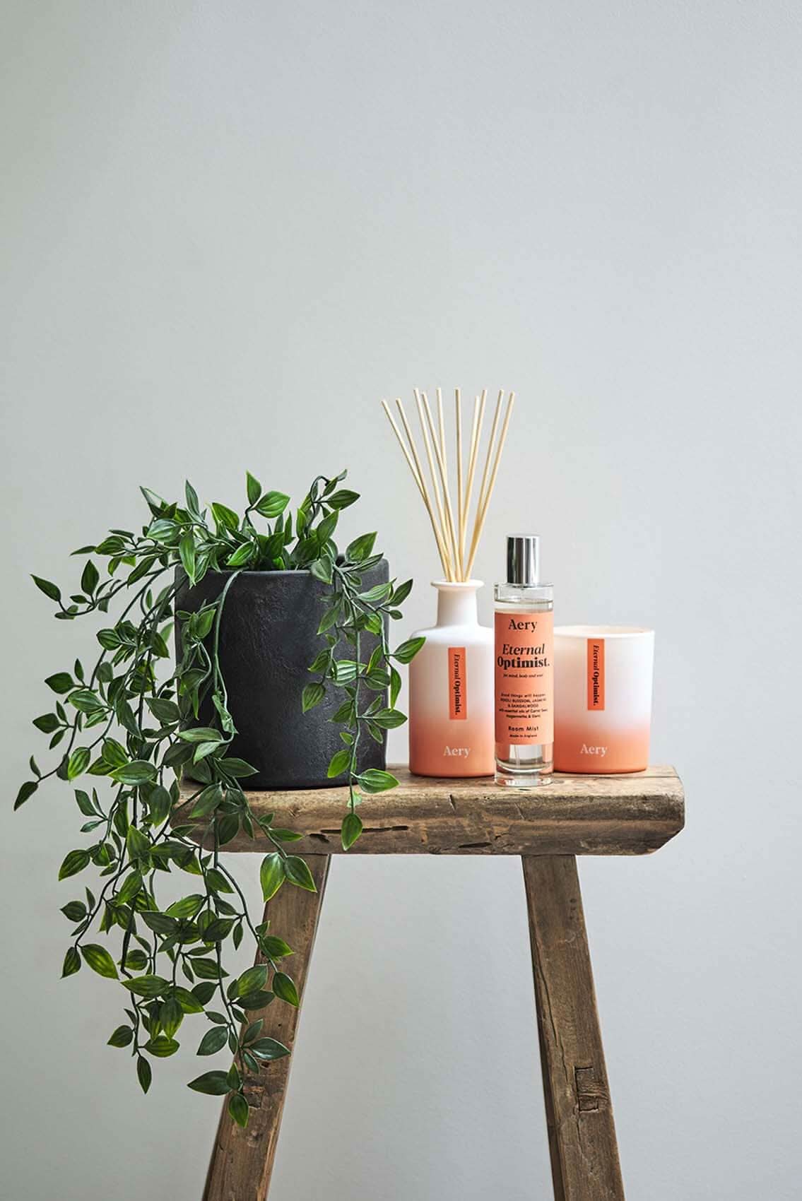 Orange Eternal Optimist room mist displayed by Aery displayed next to Eternal Optimist diffuser and candle on wooden stall