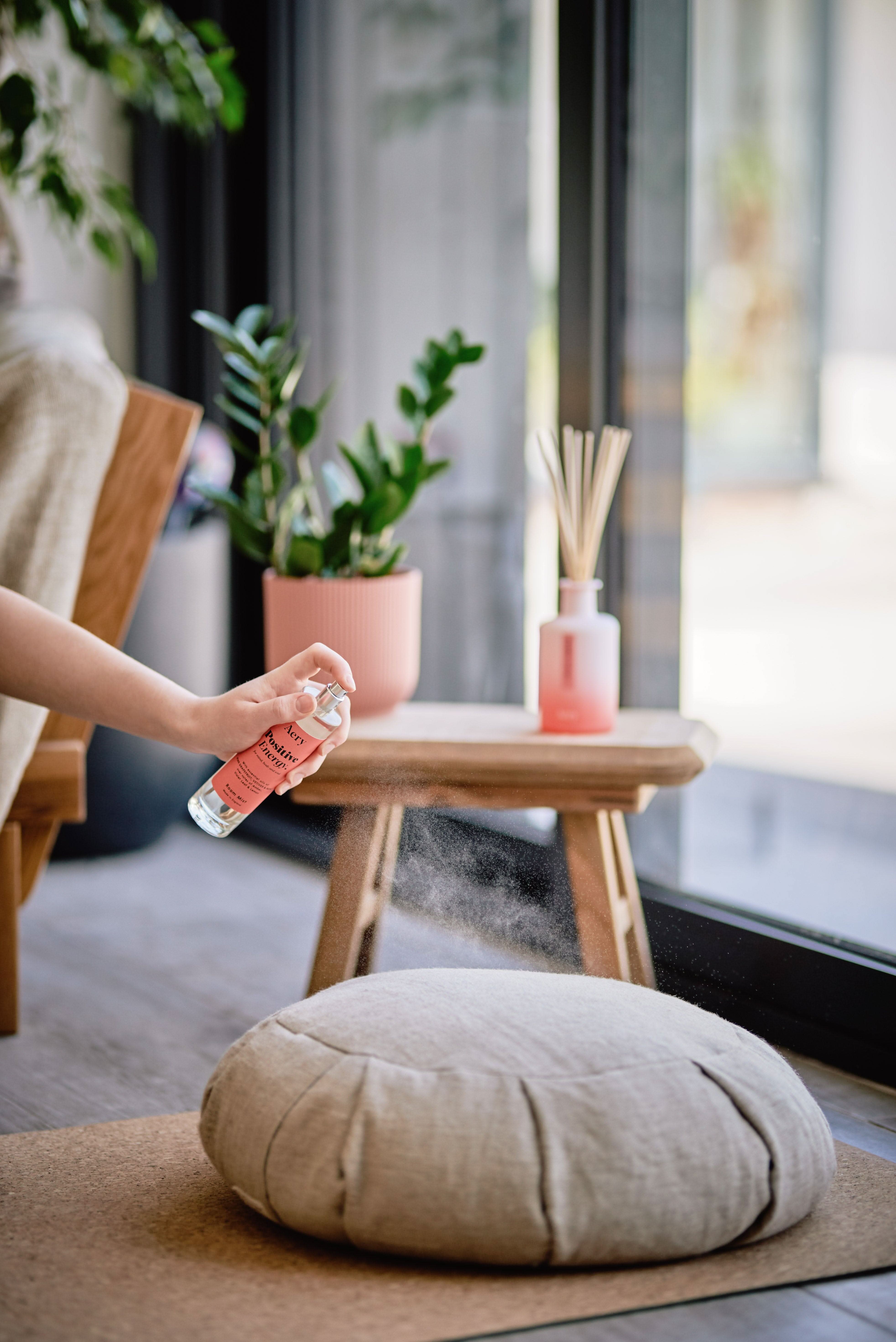 Orange Positive Energy room mist by Aery displayed in hand with plant pot and diffuser