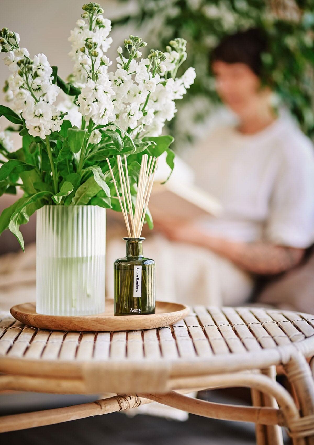 Green Bamboo diffuser by aery displayed next to glass vase of white flowers