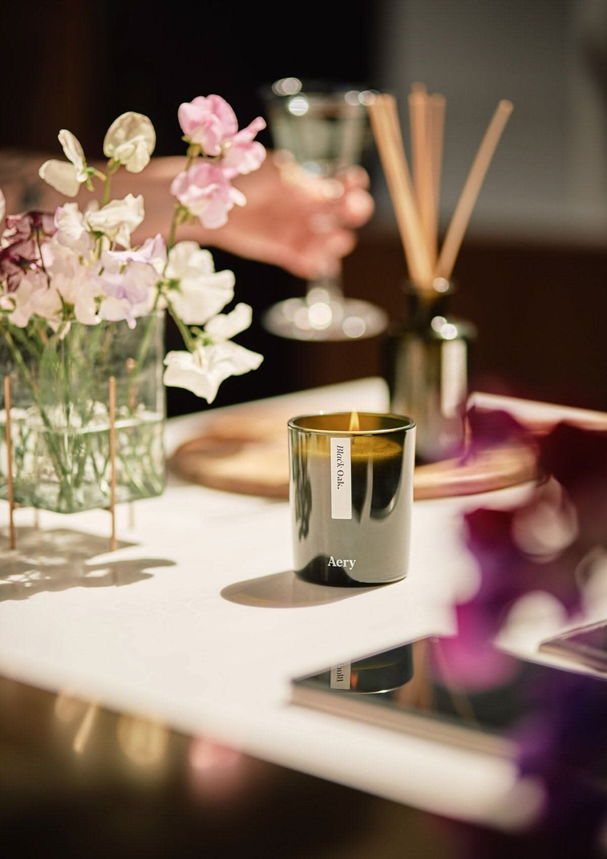 Green Black Oak candle by Aery displayed next to vase of flowers placed on kitchen work top