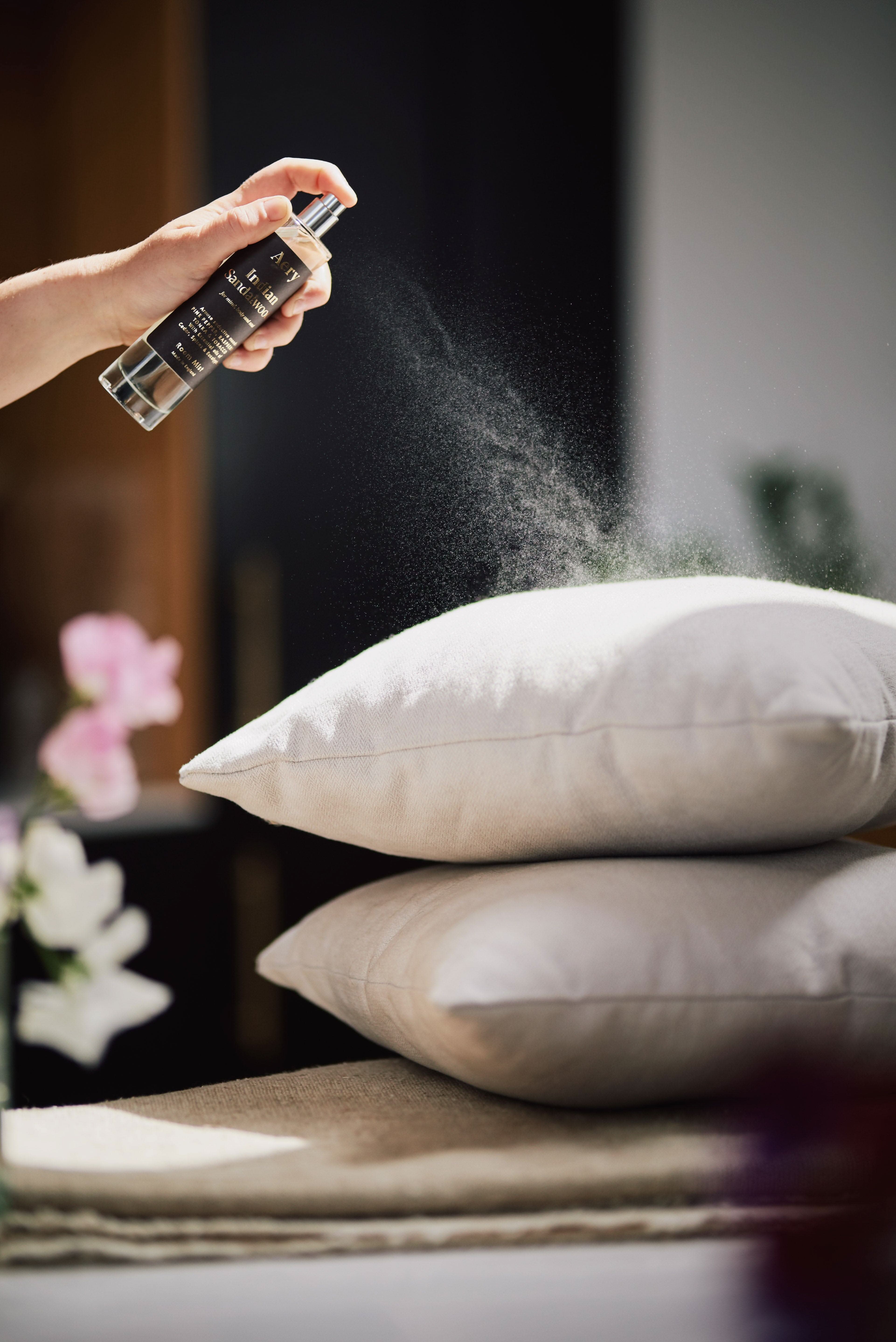 Black Indian Sandalwood room mist by Aery displayed in hand spraying grey cushions
