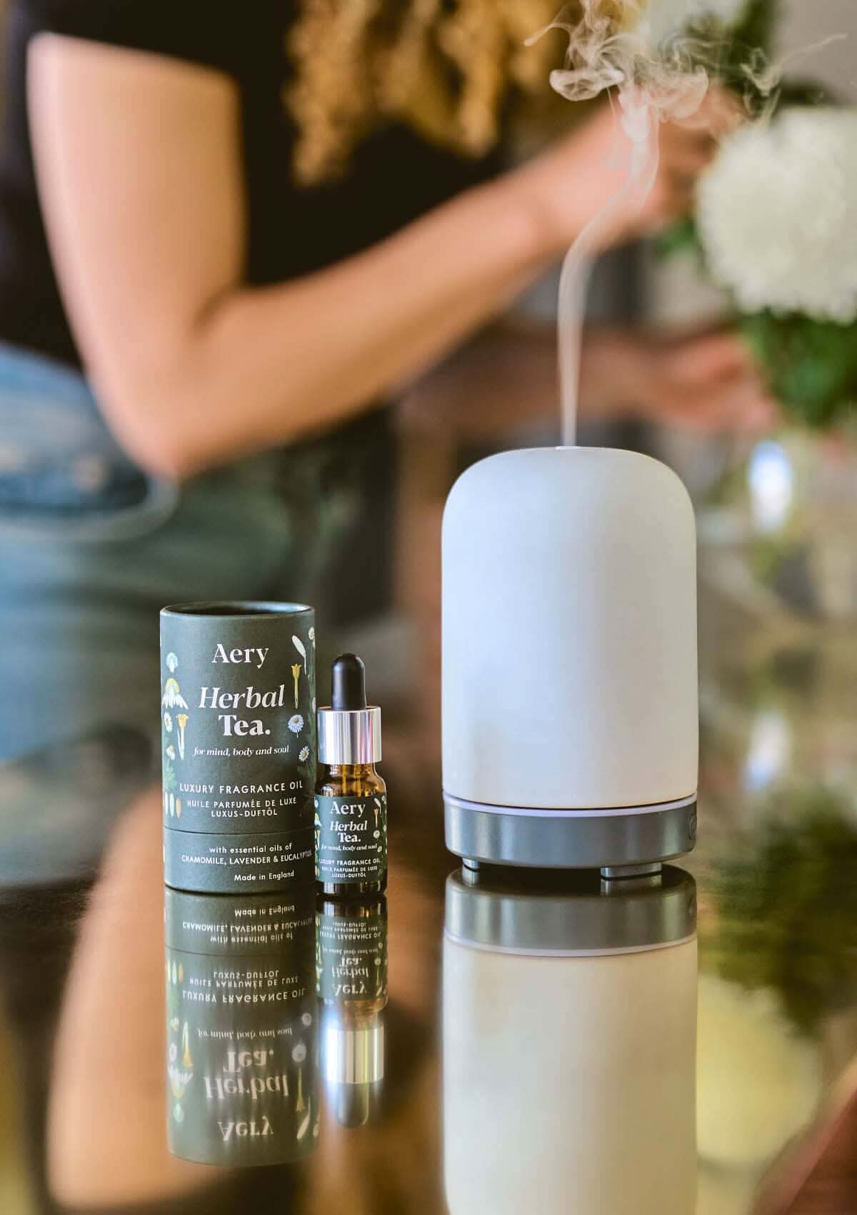 Herbal Tea Fragrance Oil by Aery displayed next to product packaging and electric diffuser on gold surface