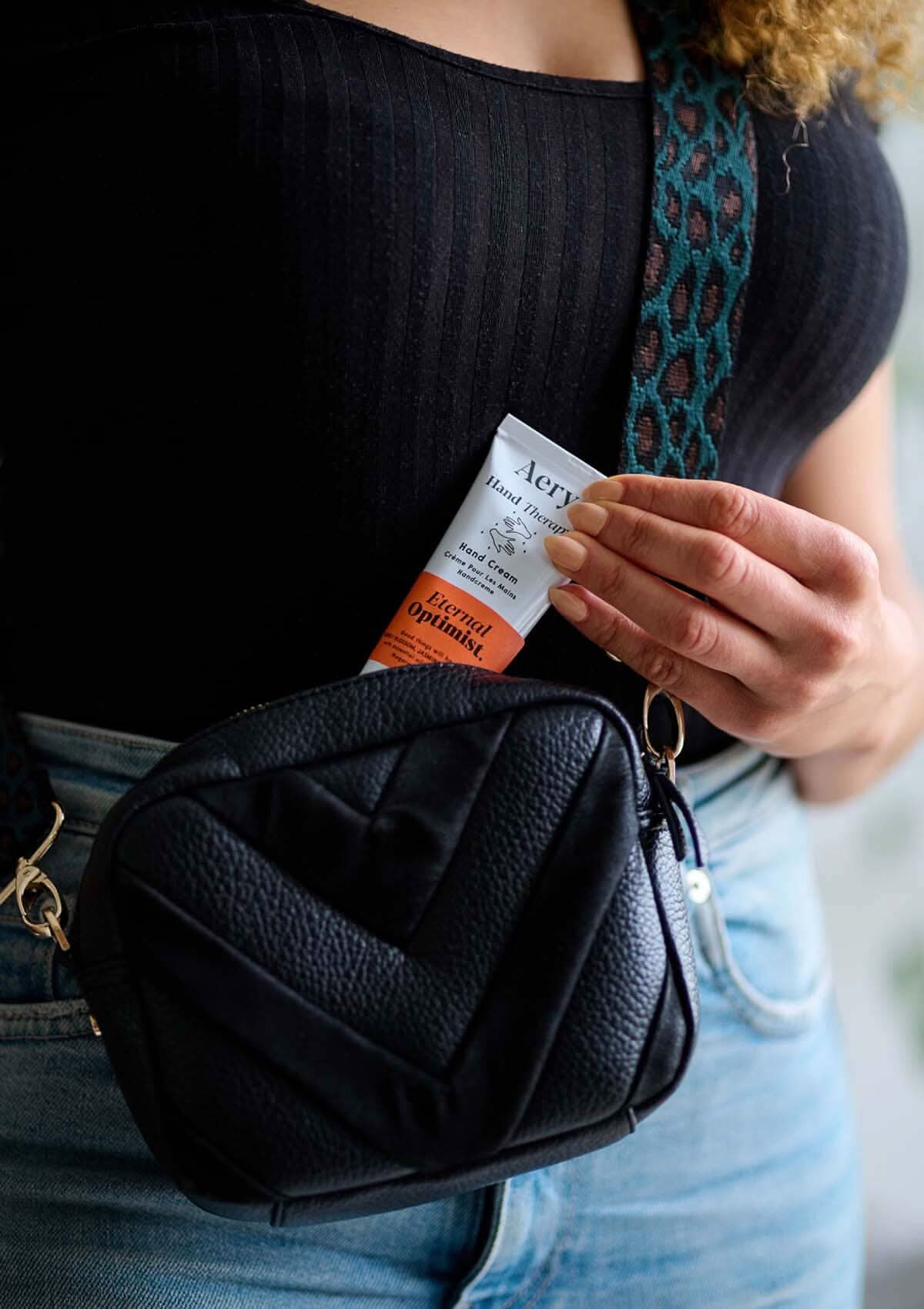 Orange Eternal Optimist hand cream displayed in hand bag being pulled out by a hand