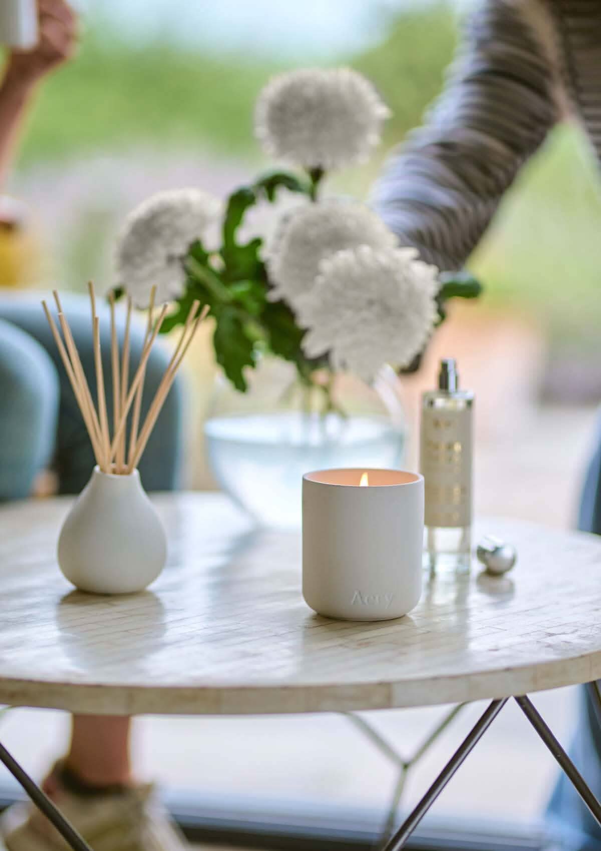 Nordic Cedar diffuser by aery displayed next to nordic cedar candle and room mist placed in front of vase of white flowers
