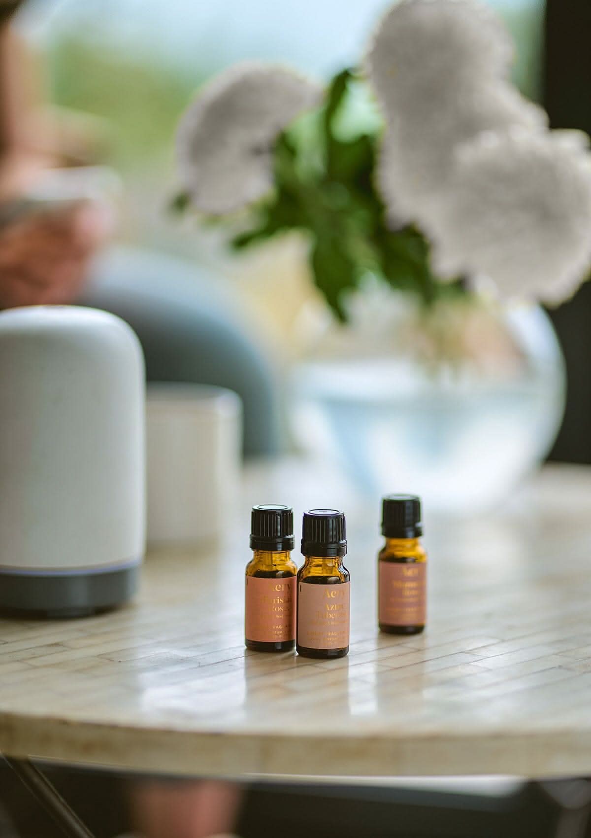 Pink Wanderlust set of three fragrance oils by Aery displayed next to electric diffuser and vase of flowers on round table
