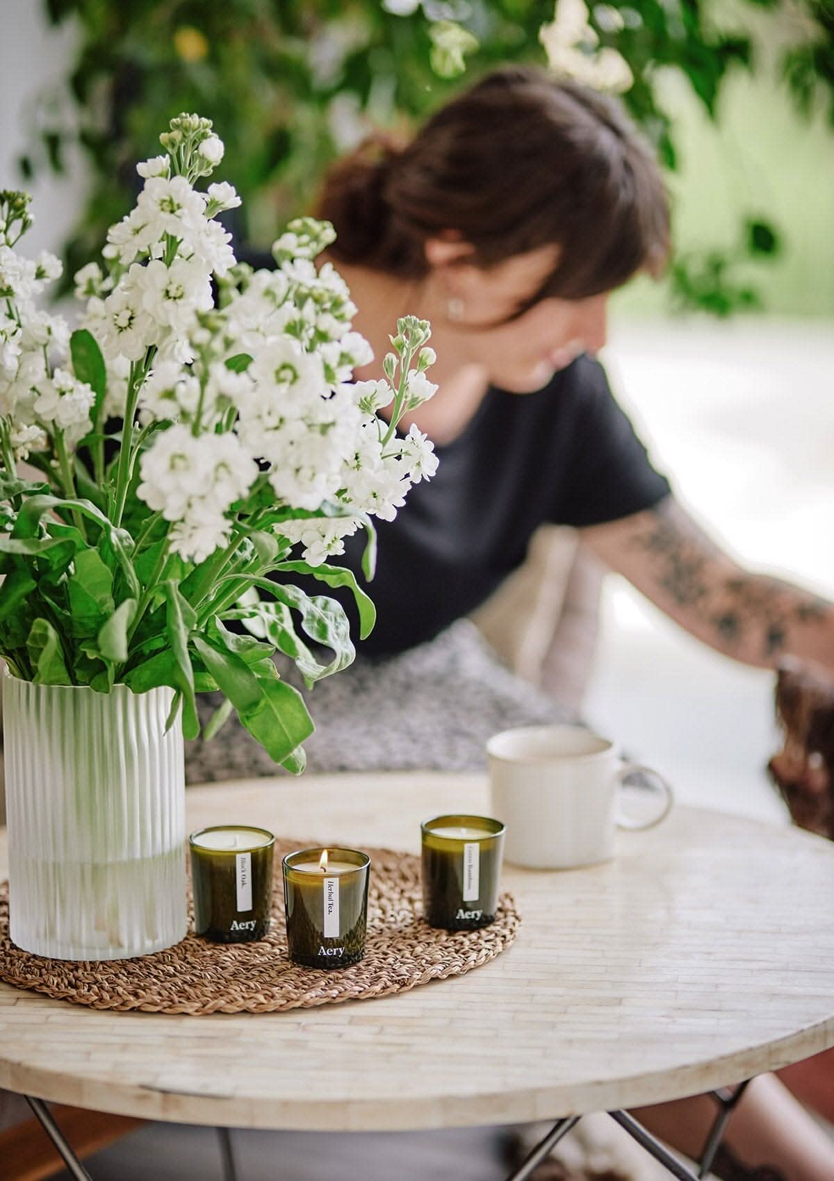 Green Botanical set of three candles by Aery displayed with vase of white flowers placed on cream table