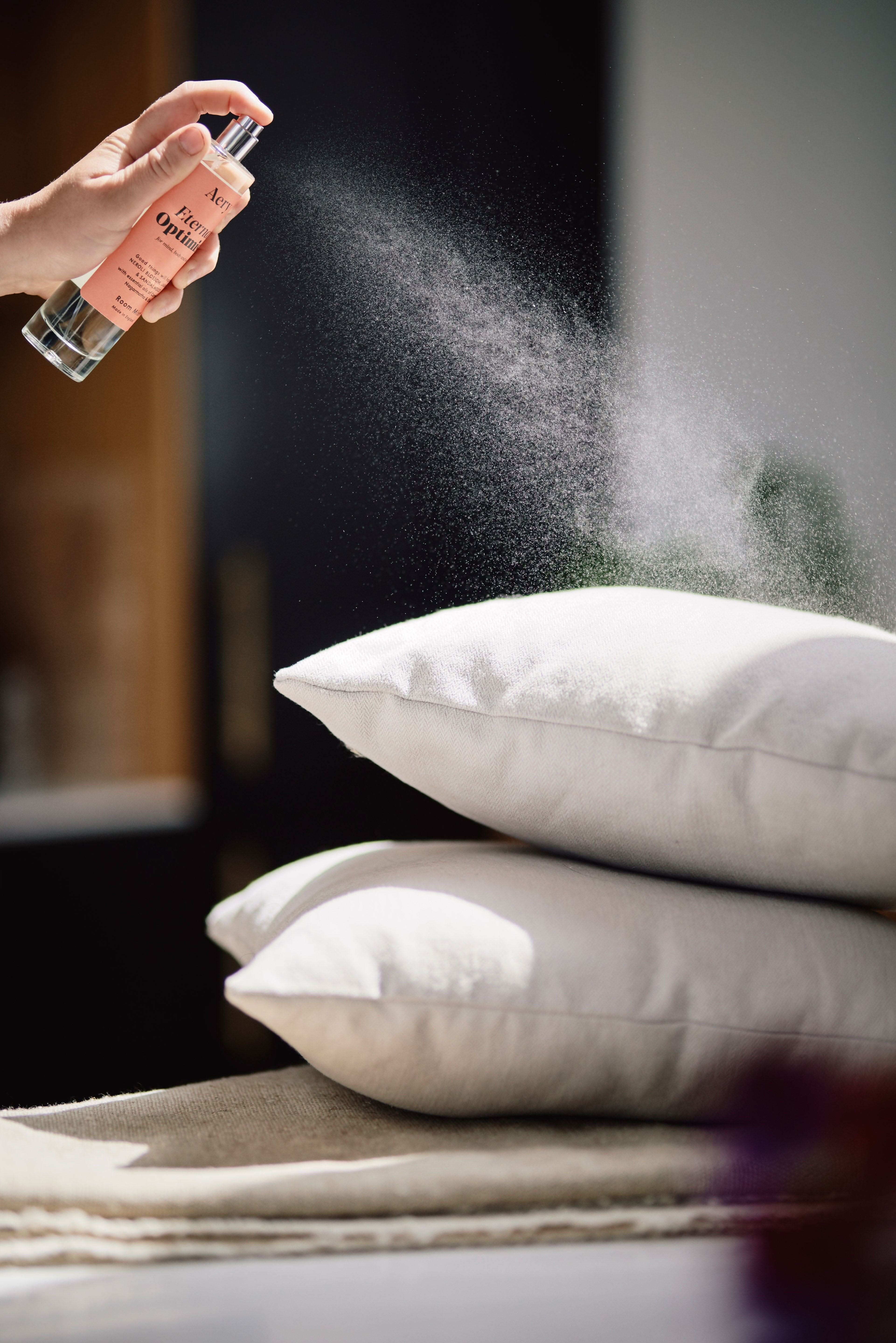 Orange Eternal Optimist room mist by Aery displayed in hand spraying grey cushions