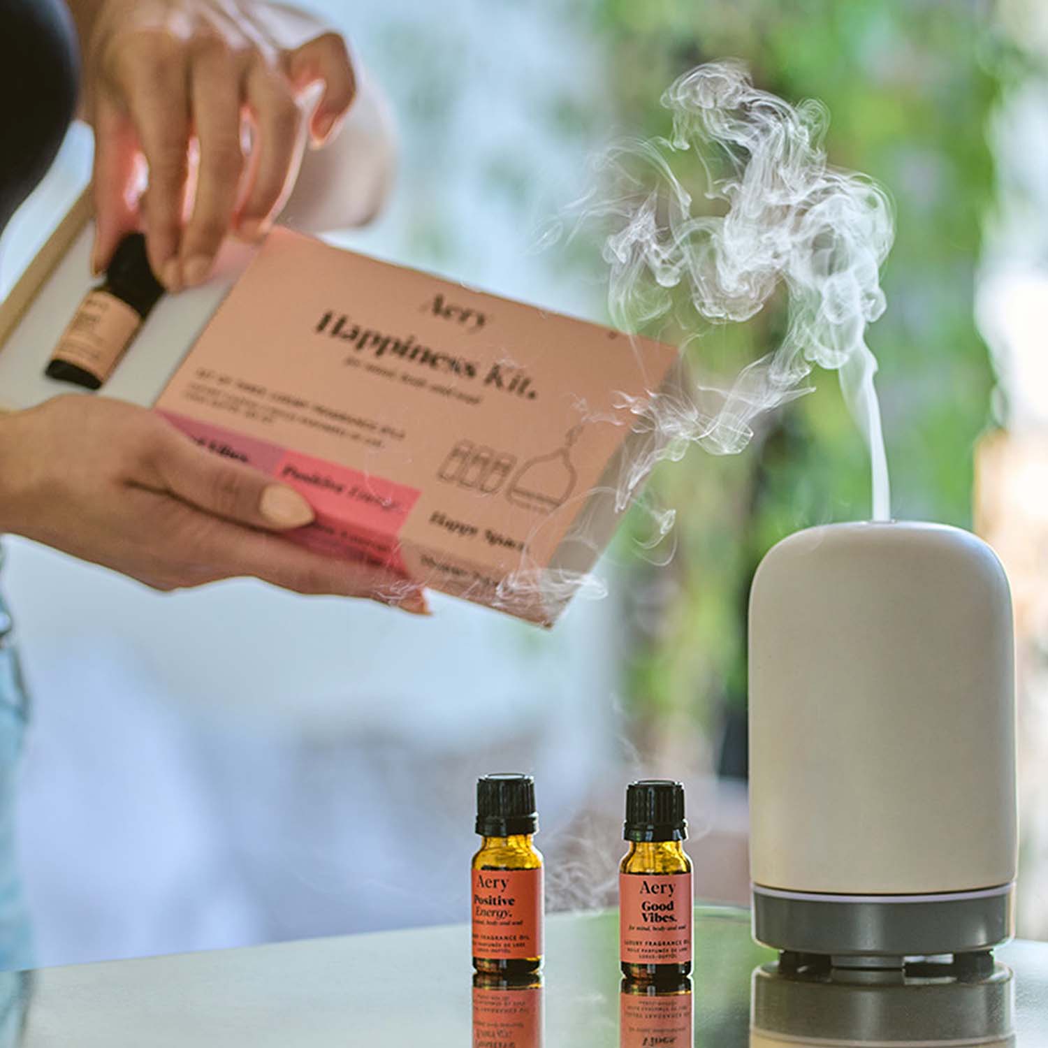 Pink Happiness Kit by Aery displayed on gold surface next to electronic diffuser product packaging held in hands