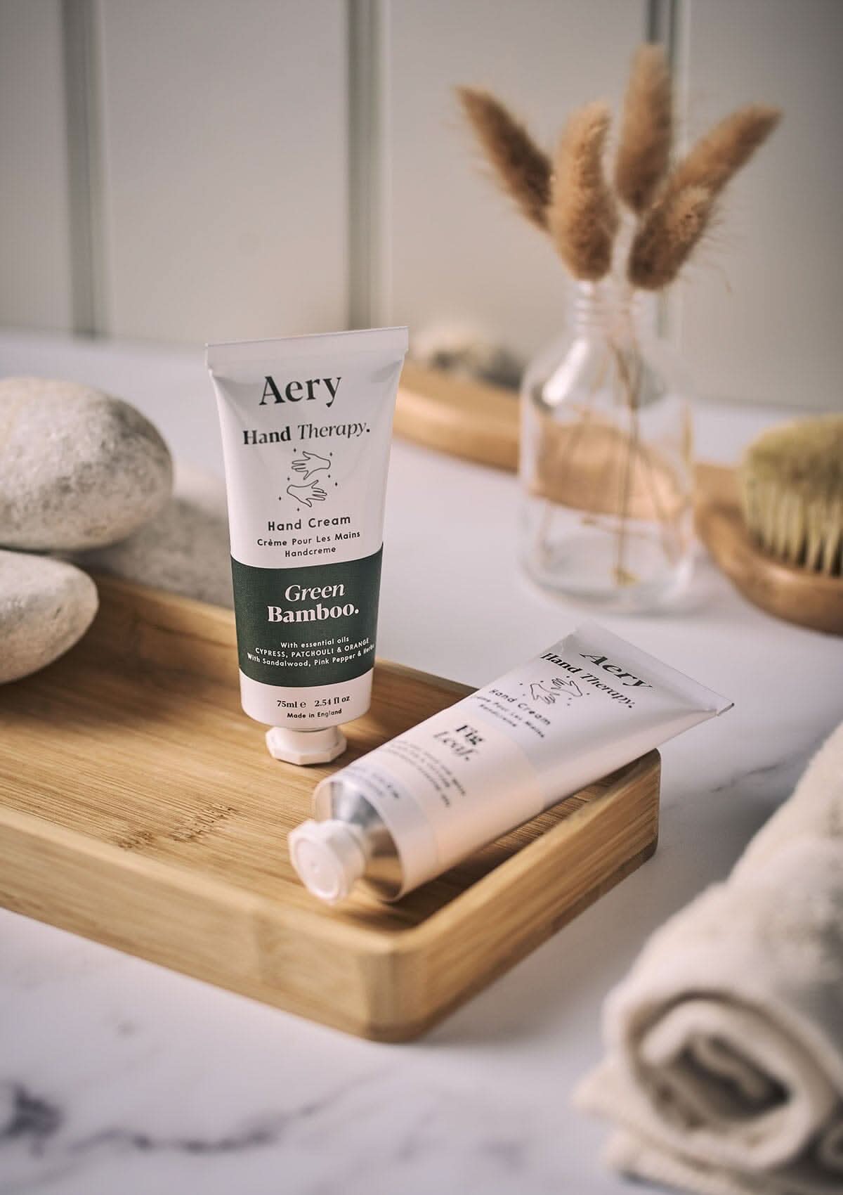 Green Bamboo hand cream by Aery displayed next to Fig leaf hand cream on wooden tray in bathroom